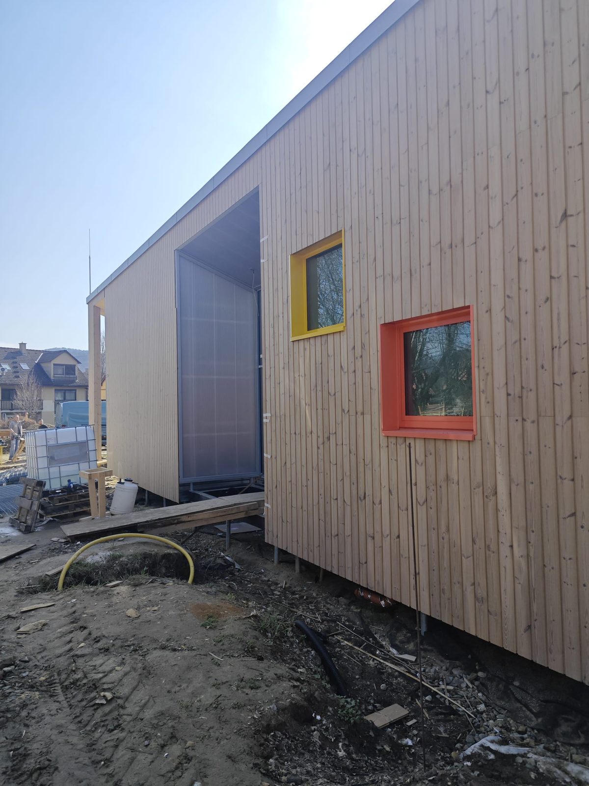 Függőleges lécburkolatú homlokzat színes ablakkávákkal